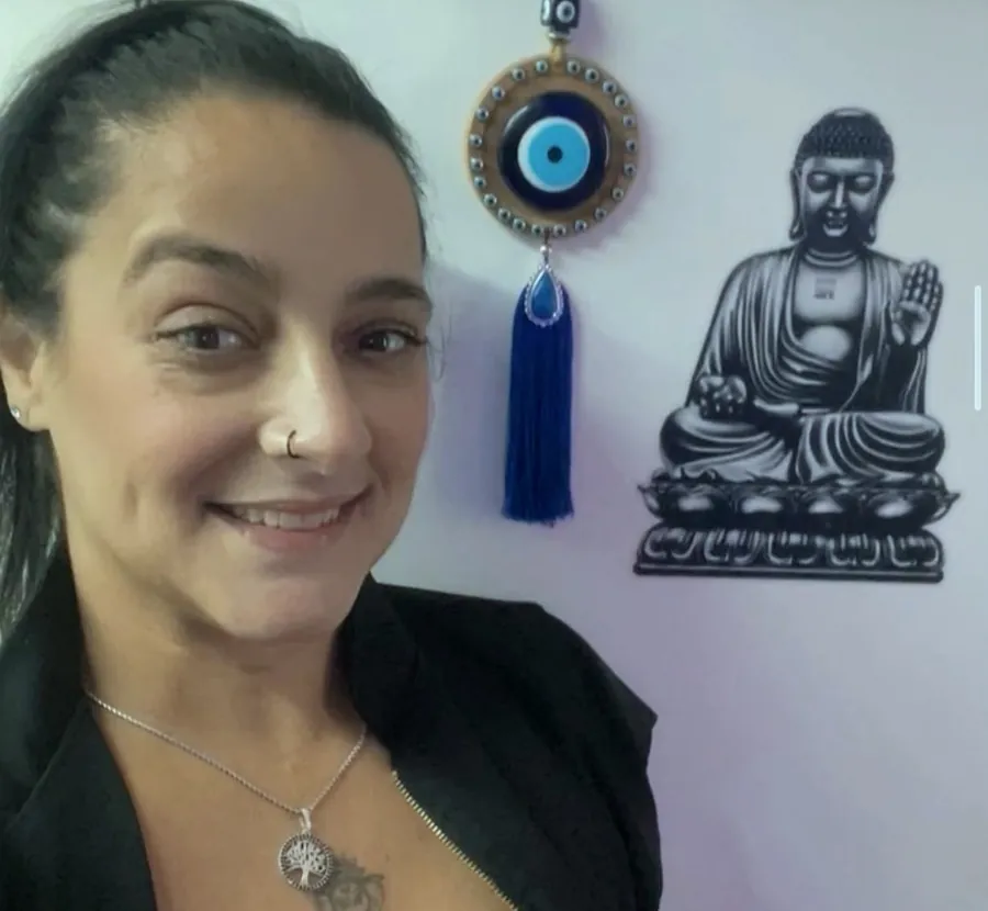 Kelly Jade no espaço de atendimento, com olho grego e imagem de Buda na parede